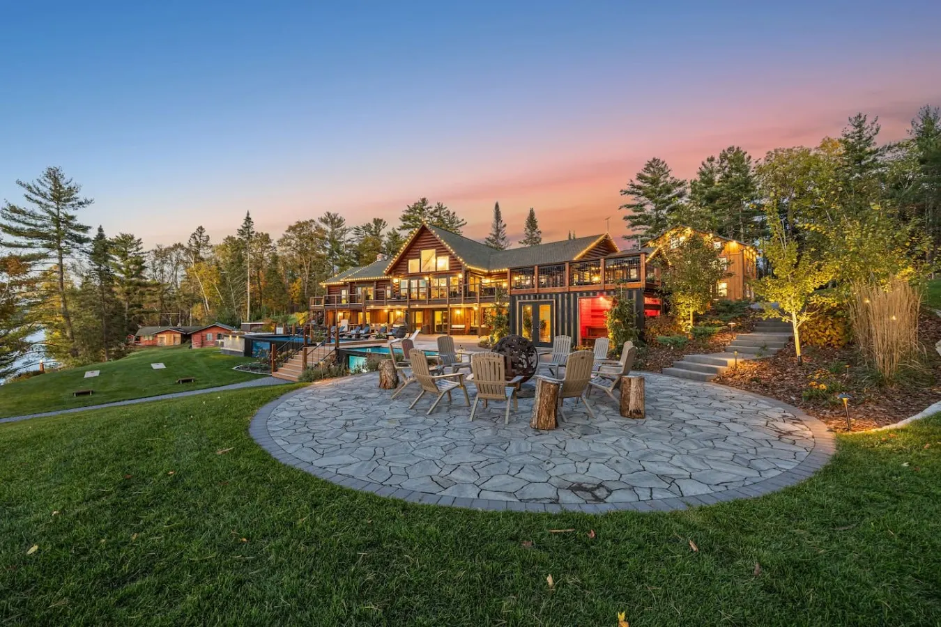 Stone fire ring with chairs in front of the lit lodge at sunset